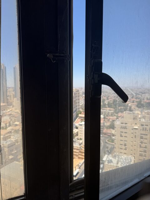 Close-up of a window handle and hinge, twenty floors above Jerusalem